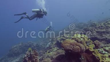 水肺潜水员潜水在美丽的珊瑚礁和鱼类的蓝色海底。 潜水员在水下游泳和观看